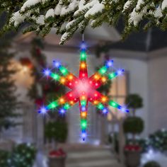 a christmas ornament hanging from a tree in front of a house with snow on the ground