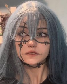 a woman with blue hair has cross drawn on her face and is looking at the camera