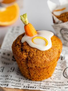 a muffin topped with icing and a carrot sitting on top of a piece of paper