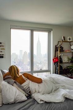 a woman is laying in bed with her head on the pillow and looking out the window