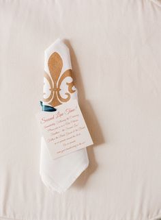 a folded napkin with a gold fleur de lys on it sitting on top of a bed