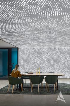 a woman sitting at a table in front of a wallpapered room with geometric designs