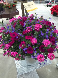 purple and pink flowers are in a bucket on a metal stand at an outdoor market