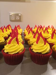 cupcakes with yellow frosting and red decorations on them sitting on a table