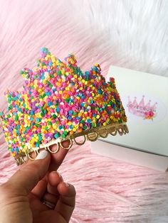 a hand is holding up a colorful sprinkle tiara in front of a box