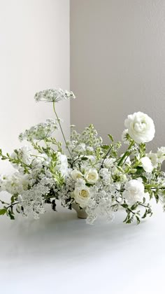 a vase filled with white flowers sitting on top of a table next to a wall