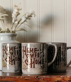 two coffee mugs sitting on top of a table next to a vase with flowers