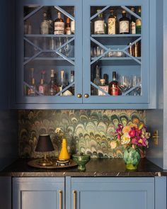 a kitchen with blue cabinets and marble counter tops in front of a wallpapered backsplash