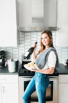 a woman is holding a bottle and some food in her hand while sitting on the stove