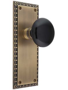 an antique brass door handle with black knob and decorative pattern on the front cover, isolated against a white background