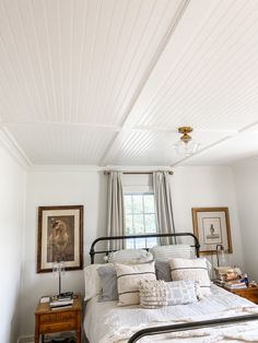 a bed sitting in a bedroom next to a window with white curtains and pillows on top of it