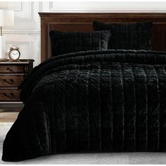 a bed with black comforter and pillows in a room next to a night stand