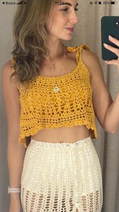 a woman taking a selfie while wearing a yellow crochet top and white skirt