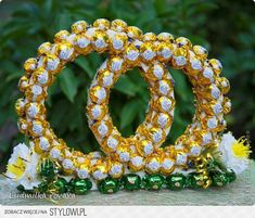 two gold and white bracelets sitting on top of each other next to flowers in front of some bushes