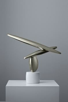 a silver sculpture sitting on top of a white table next to a gray wall with a surfboard sticking out of it