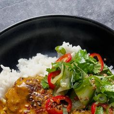 a black plate topped with rice, meat and veggies on top of it