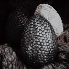 two black and white eggs sitting on top of a fur covered bedding with dark background