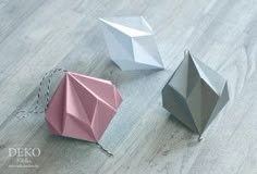 three different colored origami pieces sitting on top of a wooden floor next to each other