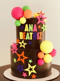 a birthday cake decorated with stars and confetti on the top is black, yellow, pink, orange and green