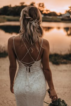 the back of a woman in a white wedding dress holding a bouquet and walking towards water