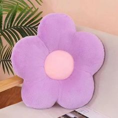 a purple flower shaped pillow sitting on top of a white table next to a plant