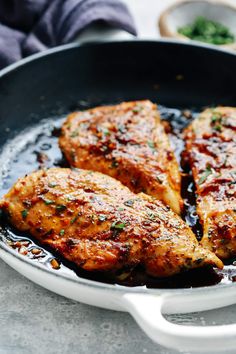 three pieces of chicken in a skillet with sauce and parsley on the side