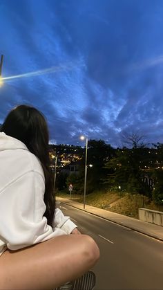 a woman sitting on the back of a motorcycle in front of a blue sky at night