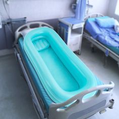 an empty hospital bed in a room with two beds on either side and blue sheets on the other