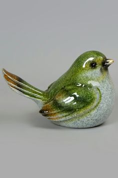 a green bird figurine sitting on top of a white table next to a gray wall