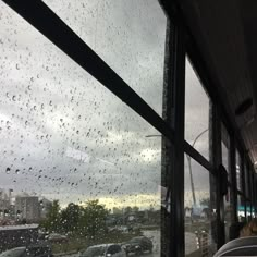 rain drops on the window of a bus as it drives down a street in front of parked cars