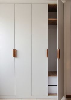 an empty closet with white cupboards and wooden handles