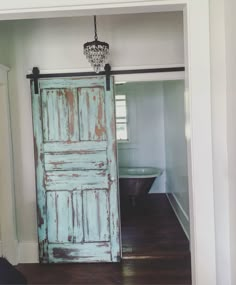 an old blue door is open to reveal a bathtub in the background and a chandelier hanging from the ceiling