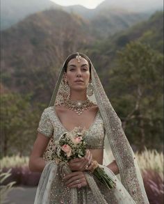 a woman in a bridal gown and veil with flowers on her head holding a bouquet