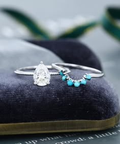 two rings sitting on top of a velvet pillow next to a ring with turquoise beads