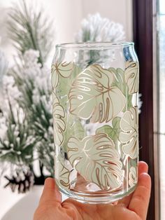 a person holding up a glass with some flowers on it in front of a potted plant