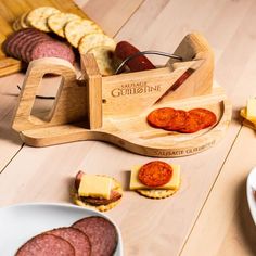 a wooden cheese board with sausages and crackers on the table next to it