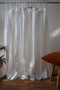 a white curtain hanging on the side of a window next to a chair and potted plant