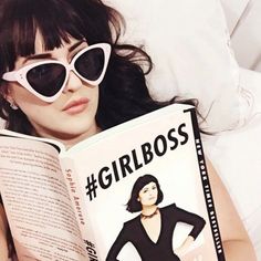 a woman laying in bed reading a book with sunglasses on her head and the caption girlboss