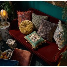 a red couch with many pillows on top of it next to a potted plant