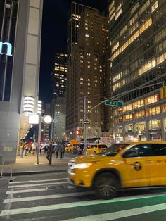 a yellow taxi cab driving down a street next to tall buildings in the city at night