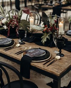 a wooden table topped with black plates and candles