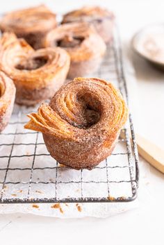 several cinnamon rolls on a cooling rack with a wooden spoon next to one and another in the background