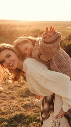 a woman holding a child in her arms while walking through a field with the sun behind her