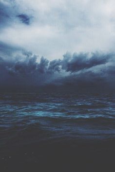 an ocean scene with dark clouds over the water and blue hues in the sky