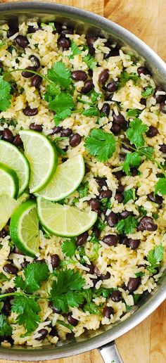 a pot filled with rice, black beans and cilantro garnished with lime wedges