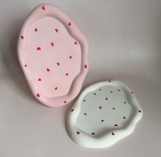 two plates with hearts painted on them sitting next to each other, one is white and the other is pink