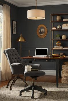 a desk with a chair, laptop and bookshelf in front of a window