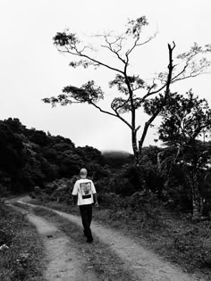 a man walking down a dirt road next to a tree