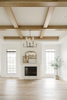 an empty living room with white walls and wood beams on the ceiling is lit by two candle chandeliers