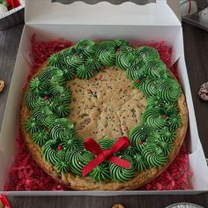 a cookie cake in a box with green frosting and red ribbon around the edges